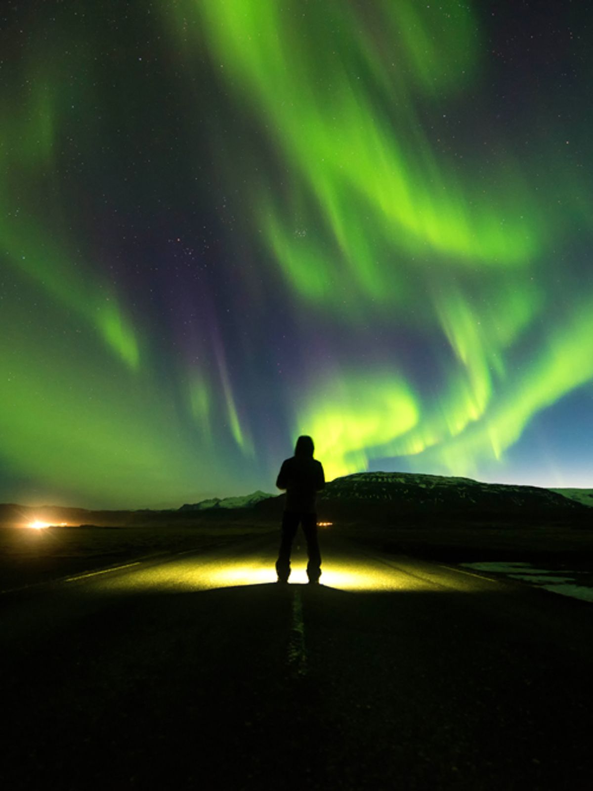 Una persona de pie sobre una carretera bajo la aurora boreal.