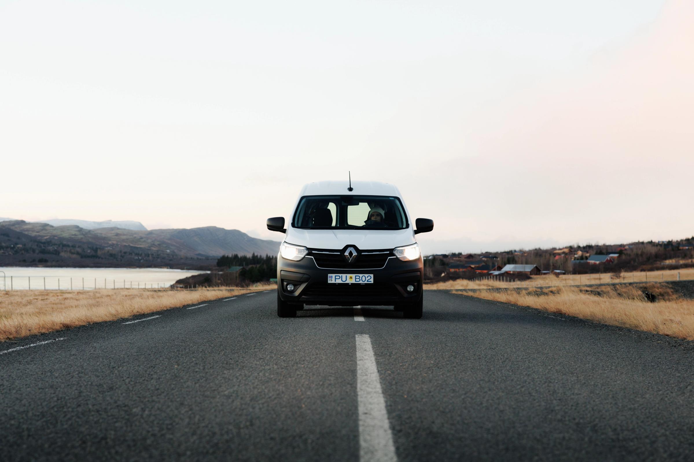 Frontalansicht eines kompakten Campervans auf einer asphaltierten Straße an einem See, Island-Campervan