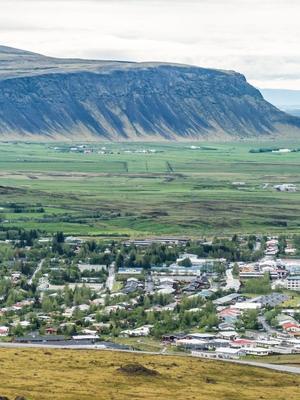 Panoramic view of a town in a green valley with a large, dark mountain cliff behind it.