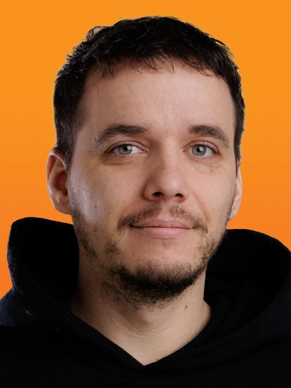 Headshot of a man with dark hair and a beard, wearing a black hoodie, smiling slightly against an orange background.