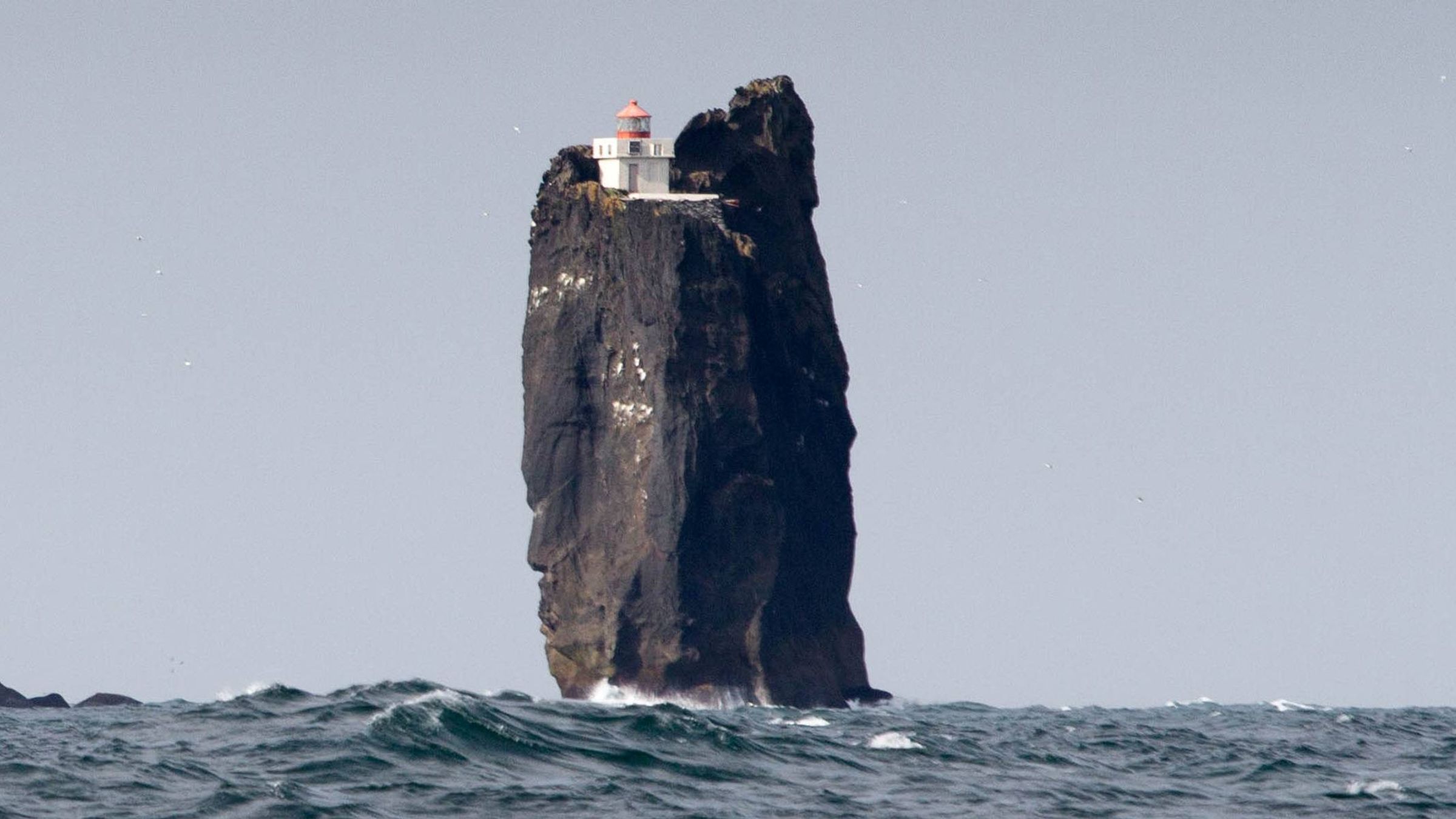 un faro blanco y rojo en la cima de una alta roca en mitad del océano