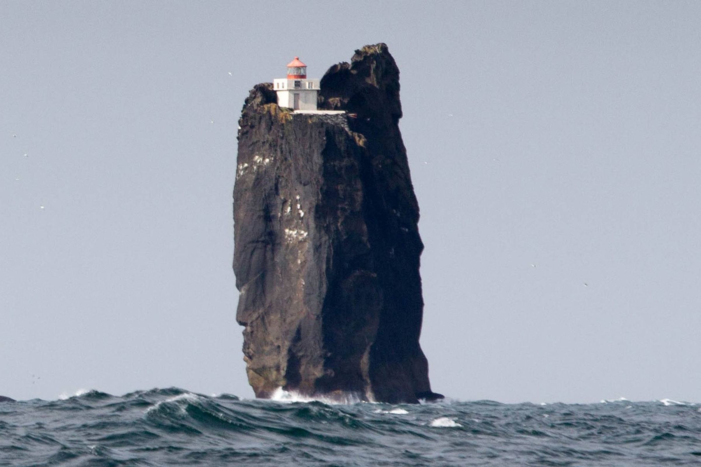 un faro blanco y rojo en la cima de una alta roca en mitad del océano
