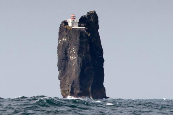 red and white lighthouse on top of a tall rock in the middle of the ocean