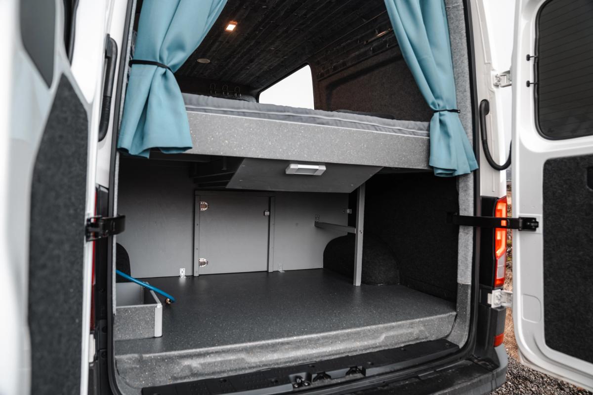 Amplio espacio de almacenamiento bajo la cama con luz de techo, visto a través de las puertas traseras abiertas