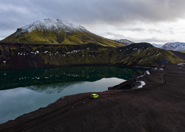 a green car is parked near a lake in the mountains