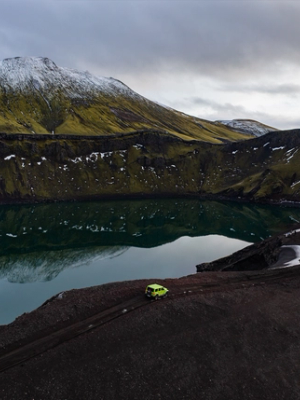 un coche verde está aparcado cerca de un lago en las montañas