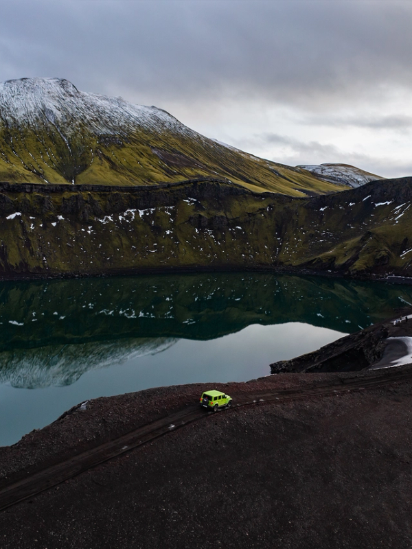 a green car is parked near a lake in the mountains