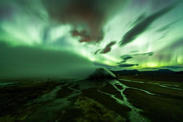 the aurora borealis is shining over a hot spring in the middle of a field .