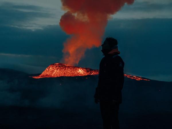 a man is standing in front of a volcano at night .