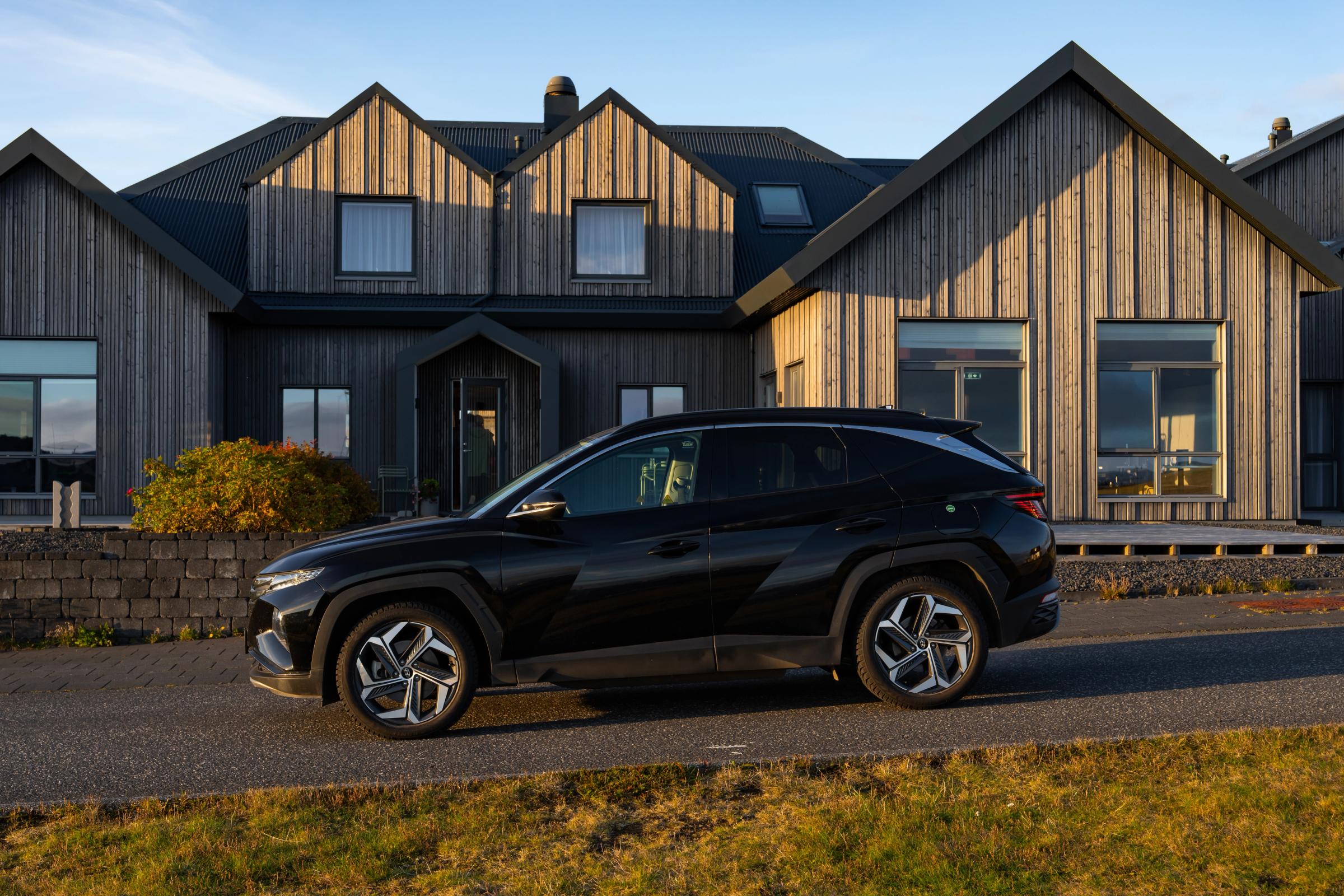 Vue de profil du Tucson Vue de profil d’un Hyundai Tucson noir sur une route goudronnée devant une maison au bardage en bois