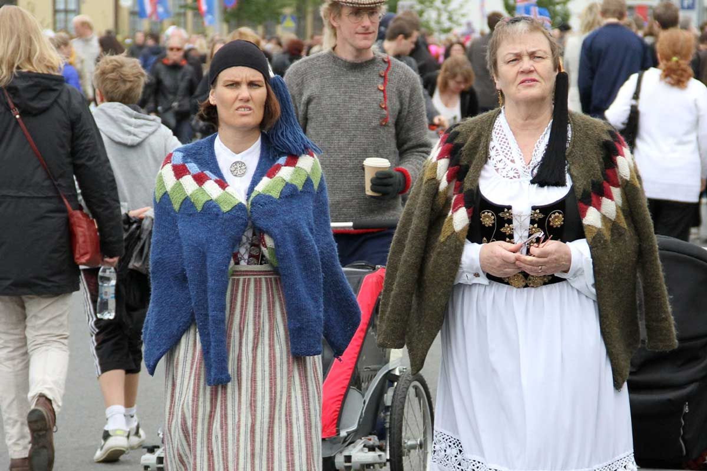 Two women in traditional Icelandic costumes walk in a crowd.