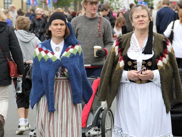 Two women in traditional Icelandic costumes walk in a crowd.