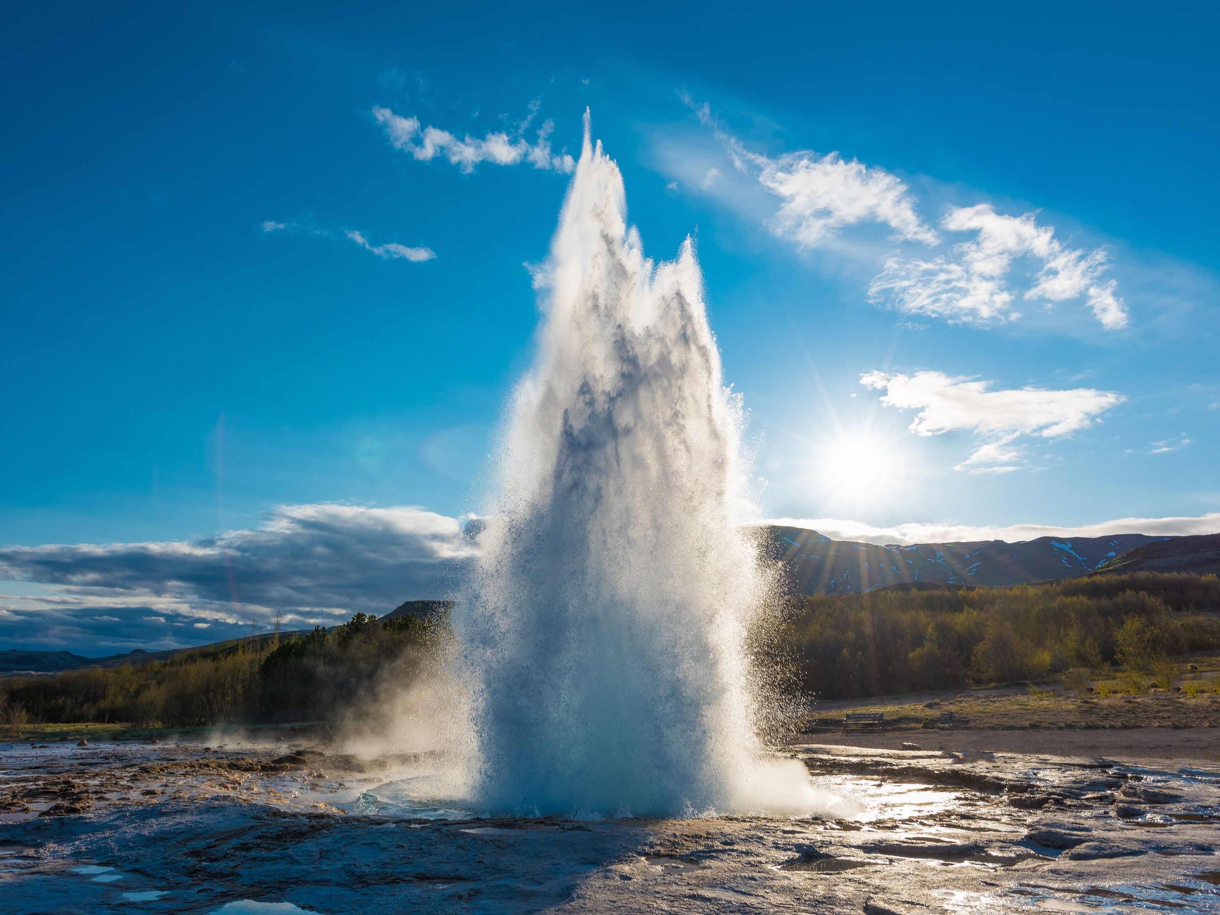 a geyser is erupting in the middle of a field with the sun shining through the clouds .