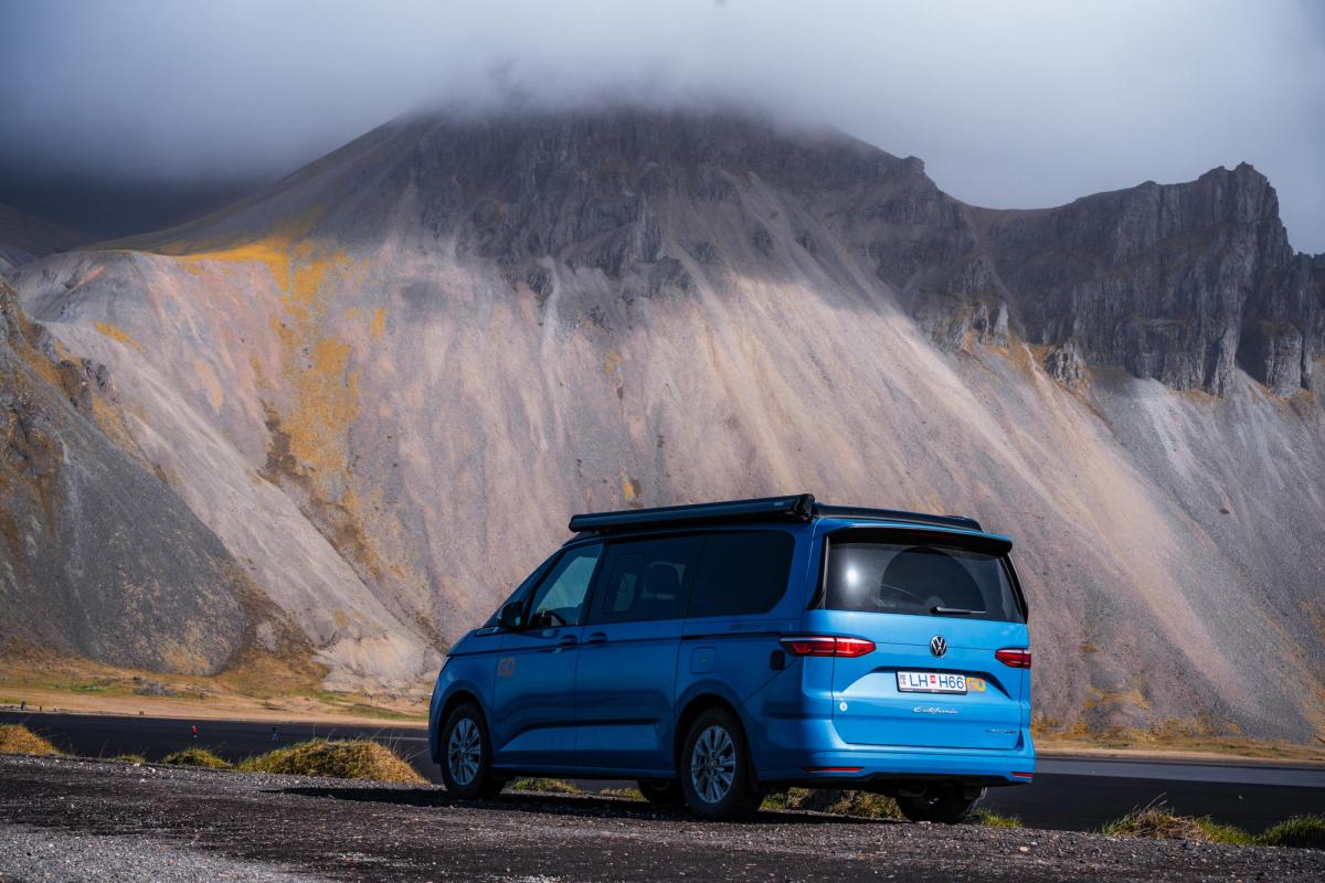 A 4x4 camper that sleeps 2 people parked below a steep mountain, campervan rental Iceland
