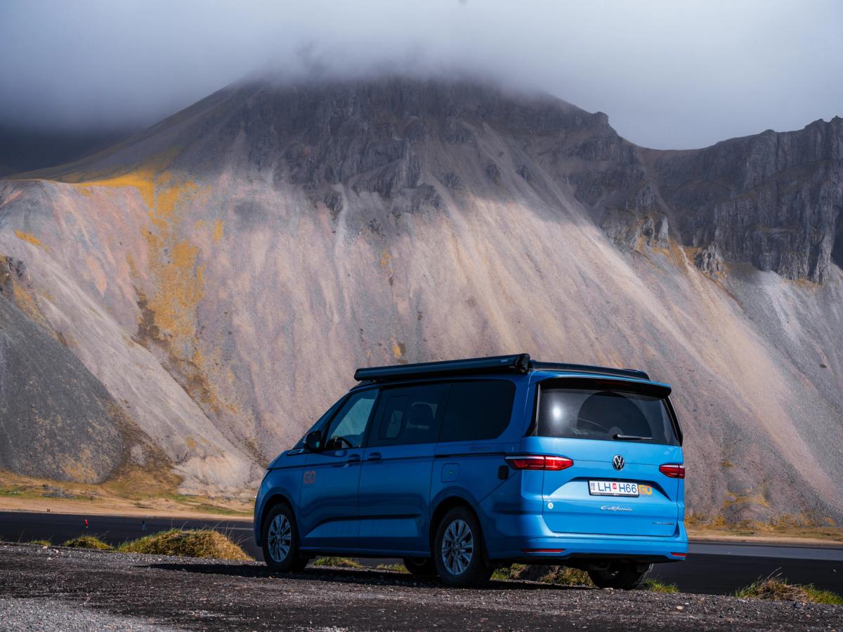 Vue arrière du camping-car 4x4 Un camping-car 4x4 pour 2 personnes garé au pied d’une montagne escarpée, location de camping-car en Islande
