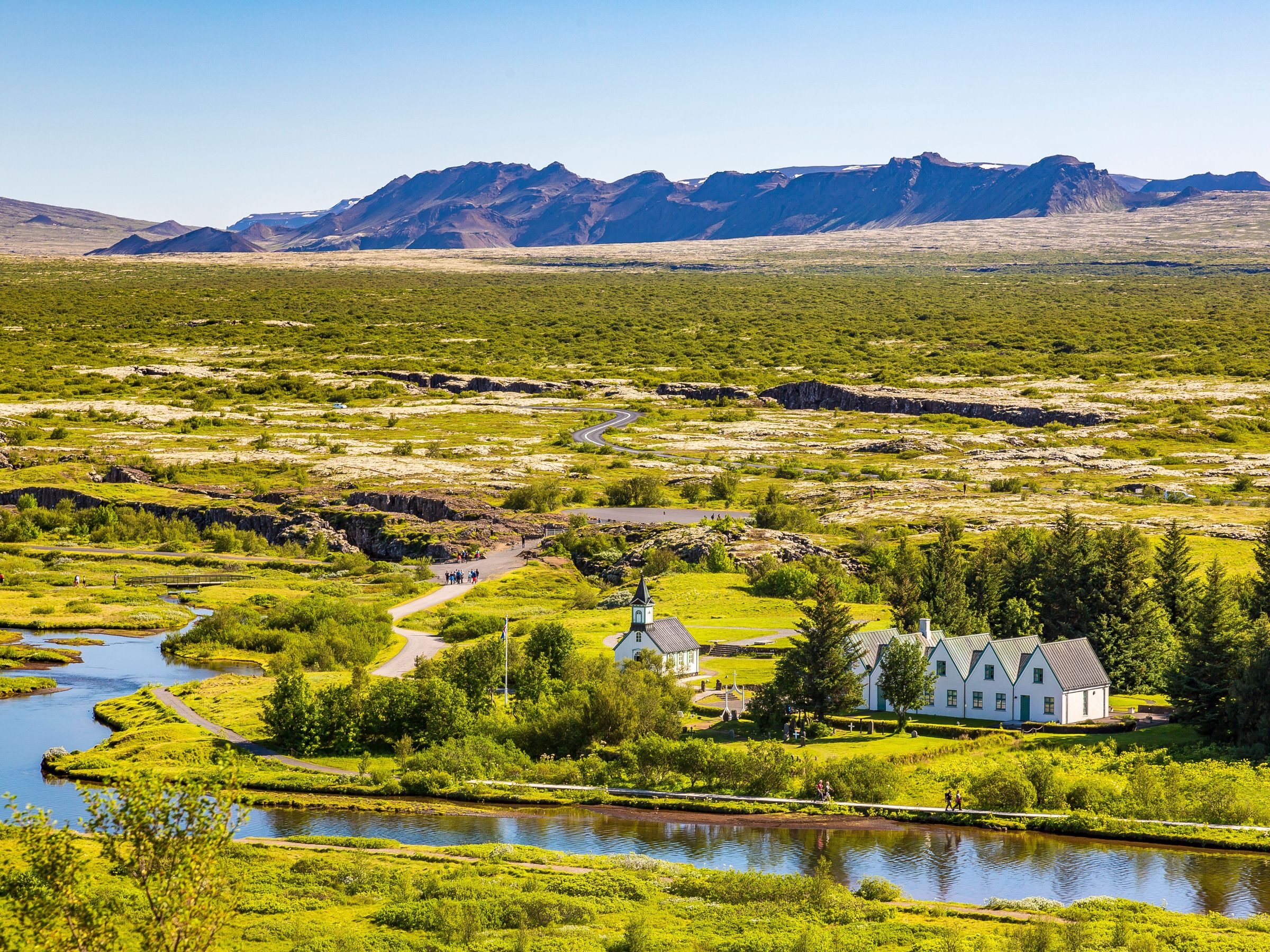a small white house sits in the middle of a grassy field next to a river .