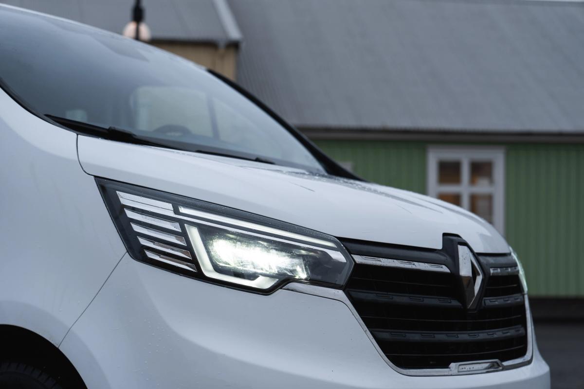 Primer plano del faro y la parrilla de un monovolumen Renault Trafic, con una casa al fondo