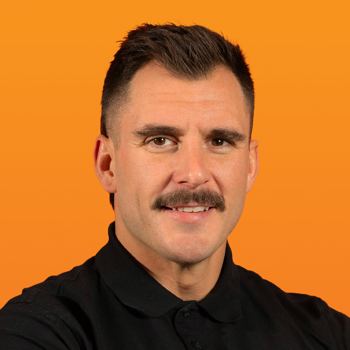 Smiling man with a mustache in a black polo shirt against an orange background.