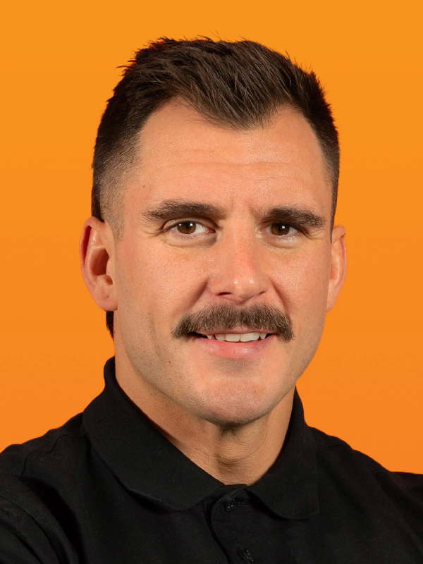 Smiling man with a mustache in a black polo shirt against an orange background.