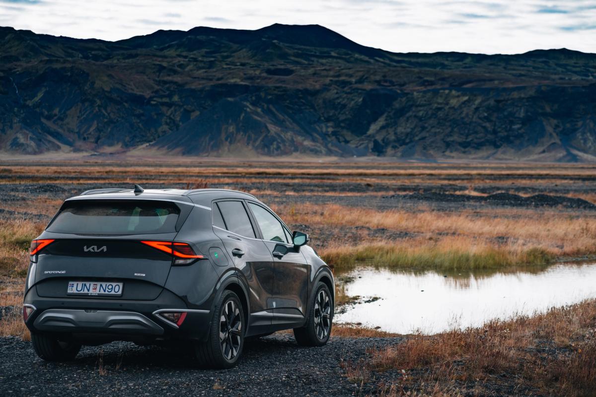 Kia Sportage-jeppi á bílastæði við opið hálendissvæði, íslenskur sjálfsakstursbílaleigubíll séður aftan frá