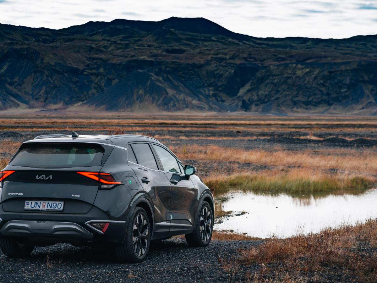 Kia Sportage Highland landslag Kia Sportage-jeppi á bílastæði við opið hálendissvæði, íslenskur sjálfsakstursbílaleigubíll séður aftan frá