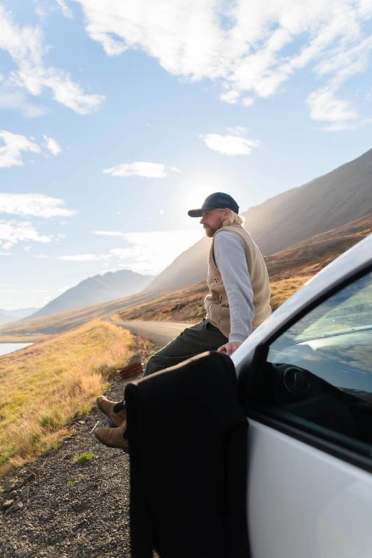 A man sitting on a rental car in iceland while the sun hits his face
