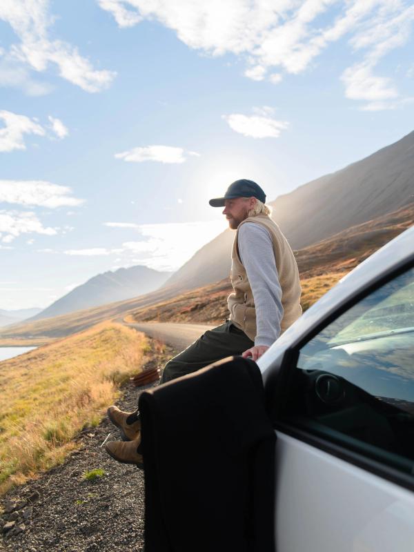A man sitting on a rental car in iceland while the sun hits his face