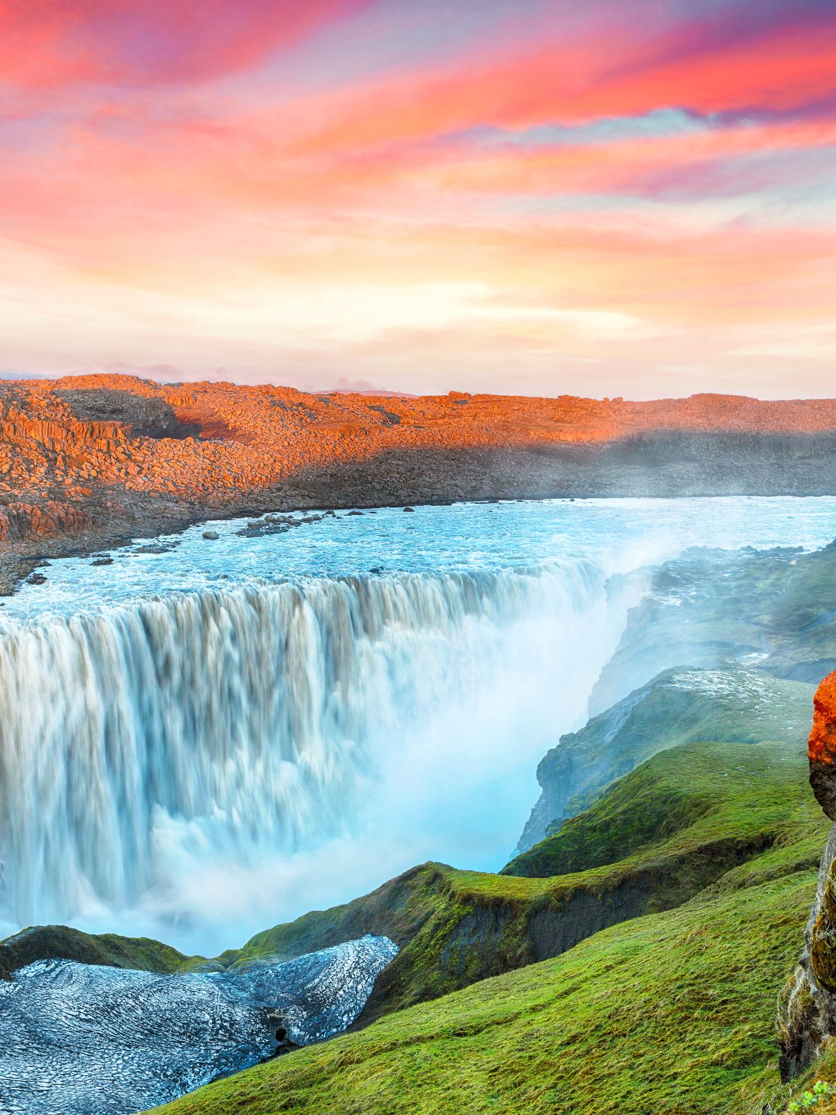 Powerful waterfall in a rocky gorge under a vibrant pink and orange sunset sky.