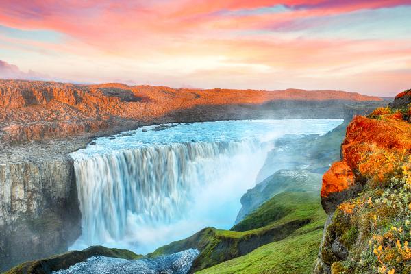 Large waterfall plunging into a rocky canyon under a vibrant sunset sky.