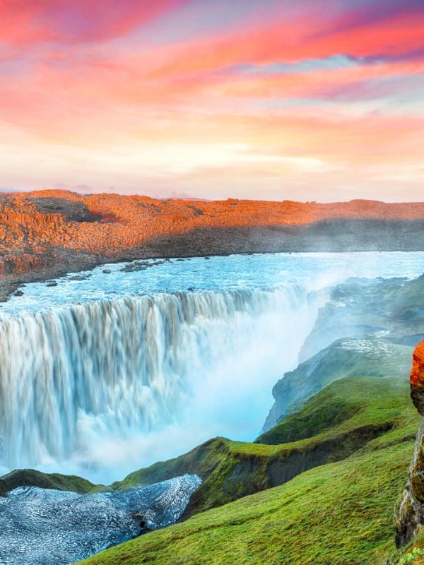 una cascada en medio de un valle con una puesta de sol de fondo.
