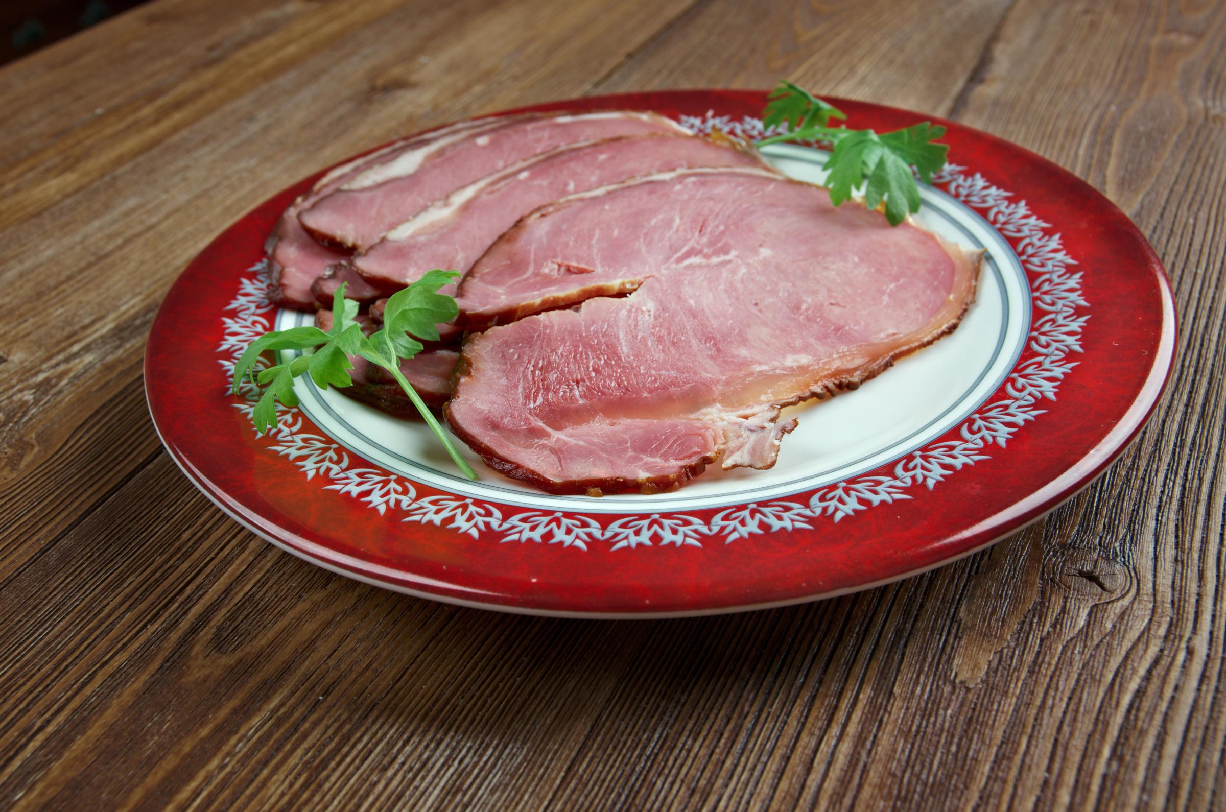 Sliced ham garnished with parsley on a red and white plate.