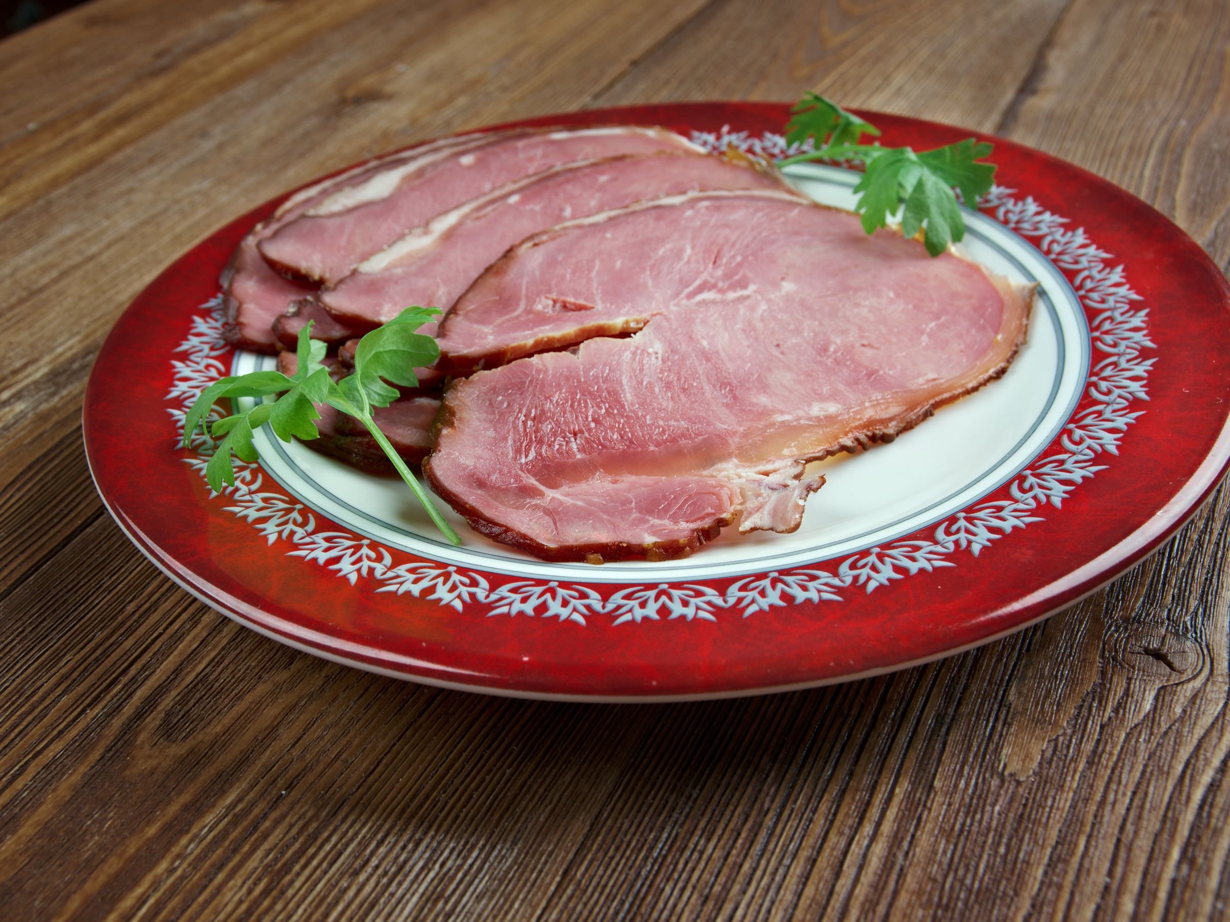 Sliced ham garnished with parsley on a red and white plate.