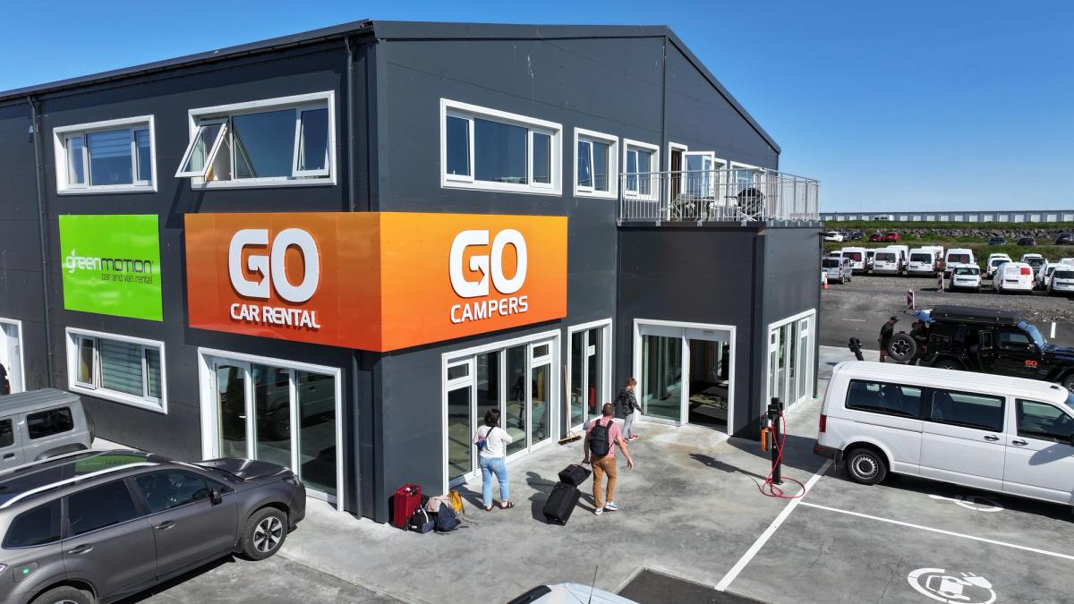 a group of people are standing outside of a go car rental building .
