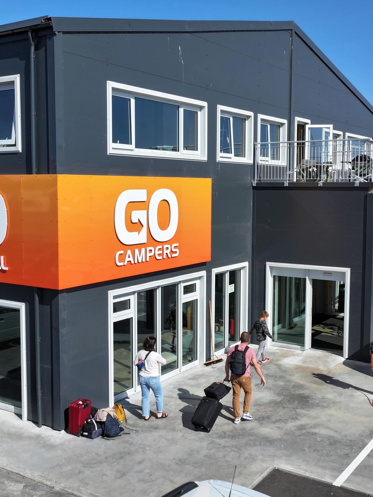 a group of people are standing outside of a go car rental building .