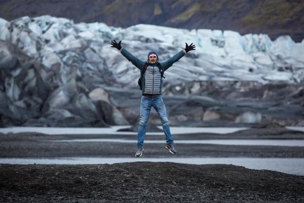 a man is jumping in the air in front of a glacier in iceland.