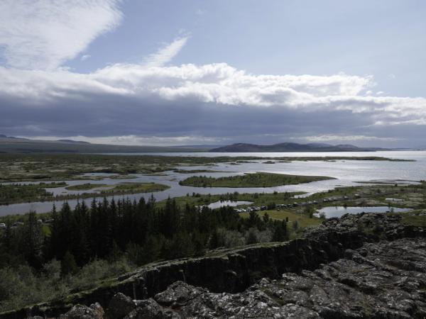 Panoramic view of a vast lake dotted with green islands, a rocky foreground, and a cloudy sky.