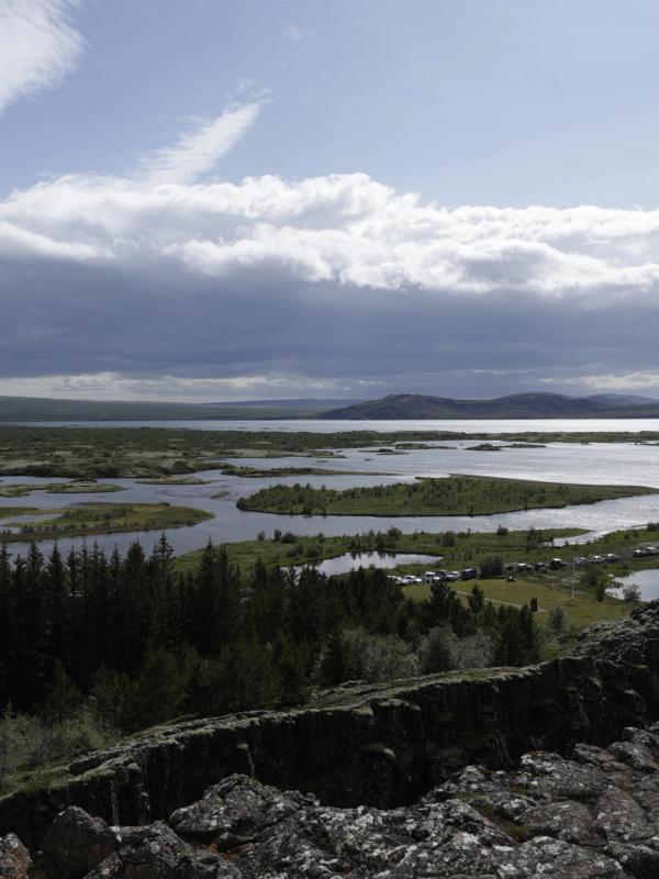 Panoramic view of a vast lake dotted with green islands, a rocky foreground, and a cloudy sky.