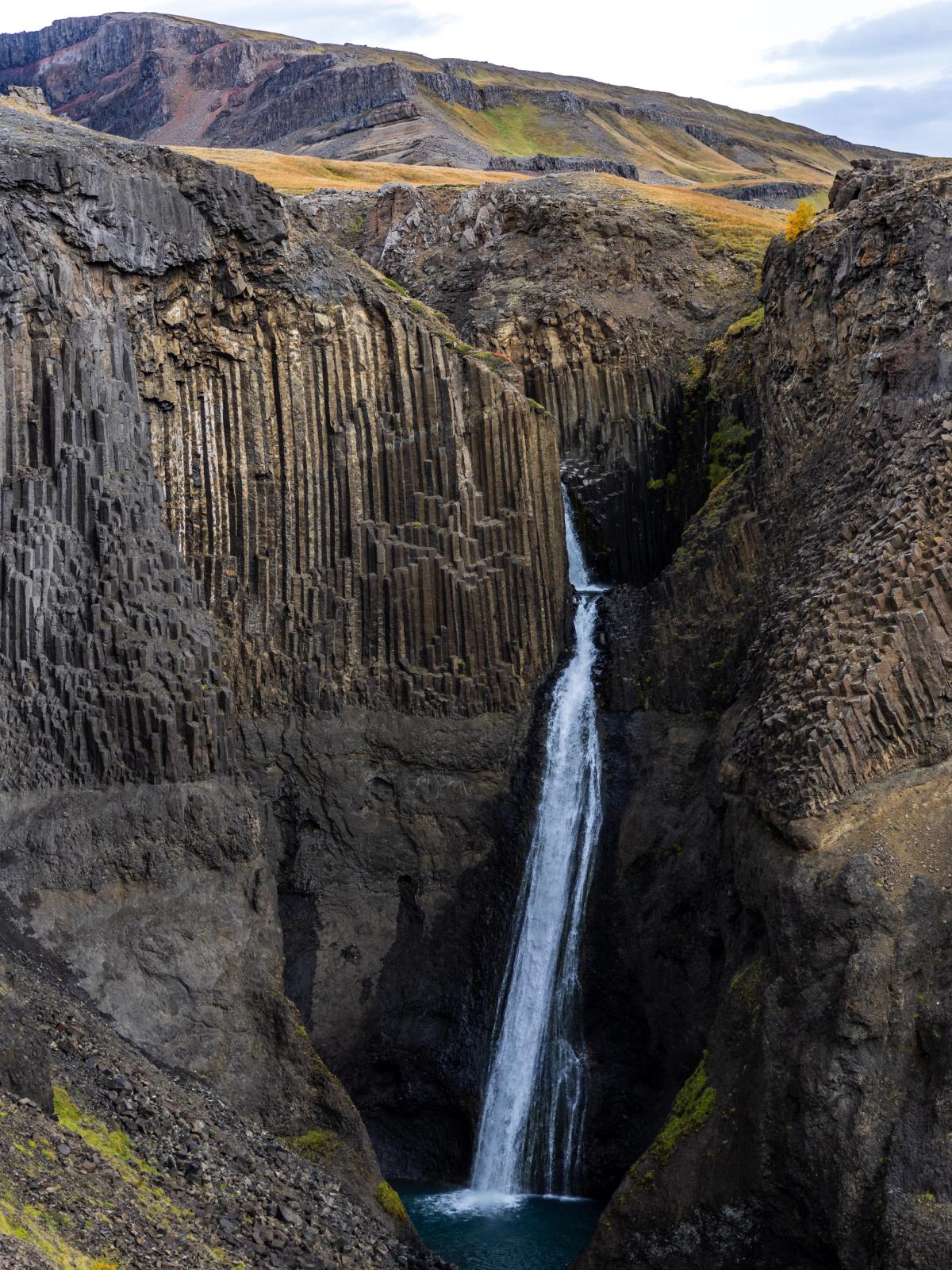 A waterfall cascades into a deep canyon with dark, vertical basalt columns lining its walls.