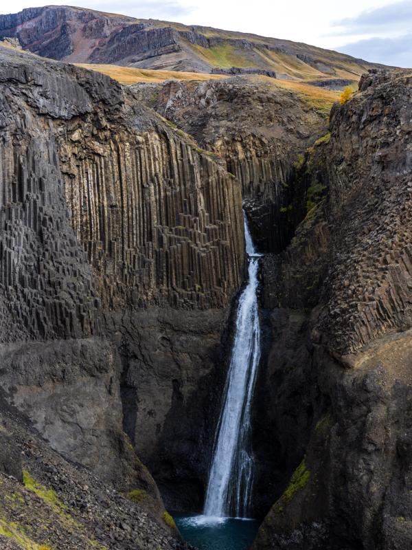 A waterfall cascades into a deep canyon with dark, vertical basalt columns lining its walls.