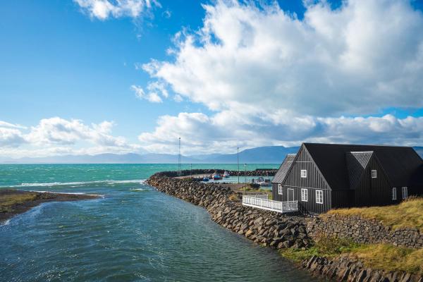 a black house is sitting on a rocky shore next to a body of water .