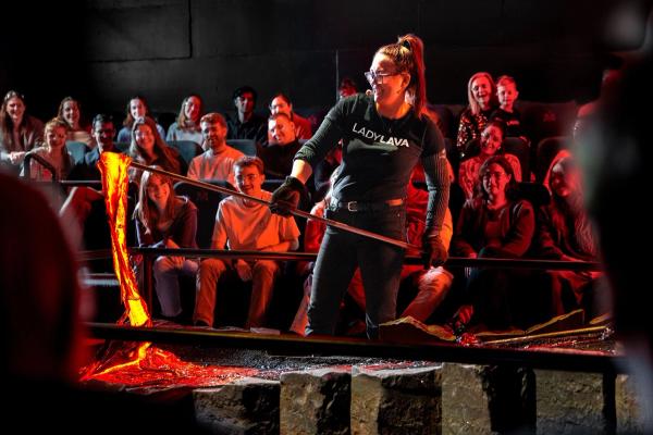 a woman is standing in front of a crowd of people holding a stick in front of a lava flow .