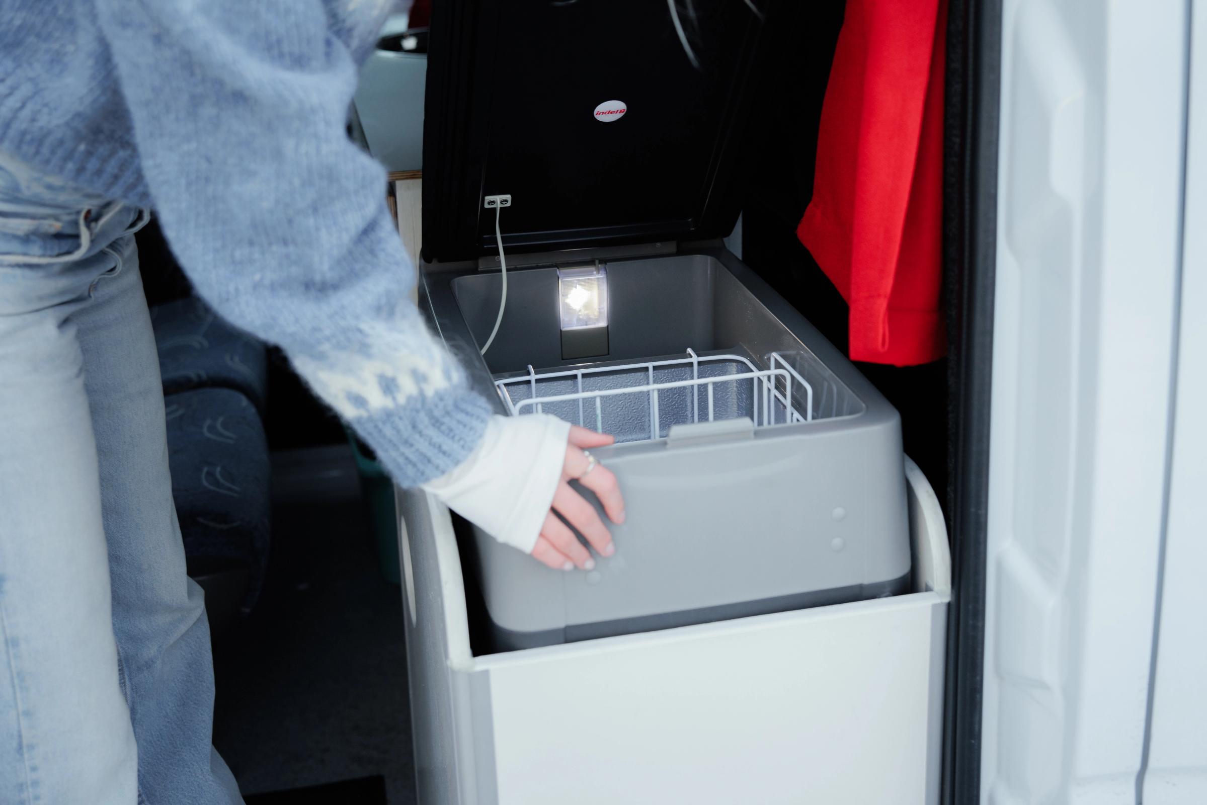 Person, die den Rand der Kühlbox mit geöffnetem Deckel festhält, neben der Seitentür