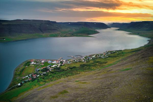 an aerial view of a lake with a small town on the shore at sunset .