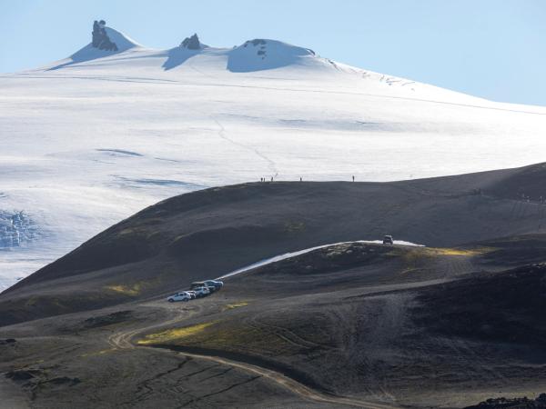 Glacier and dark volcanic hills with people and vehicles.