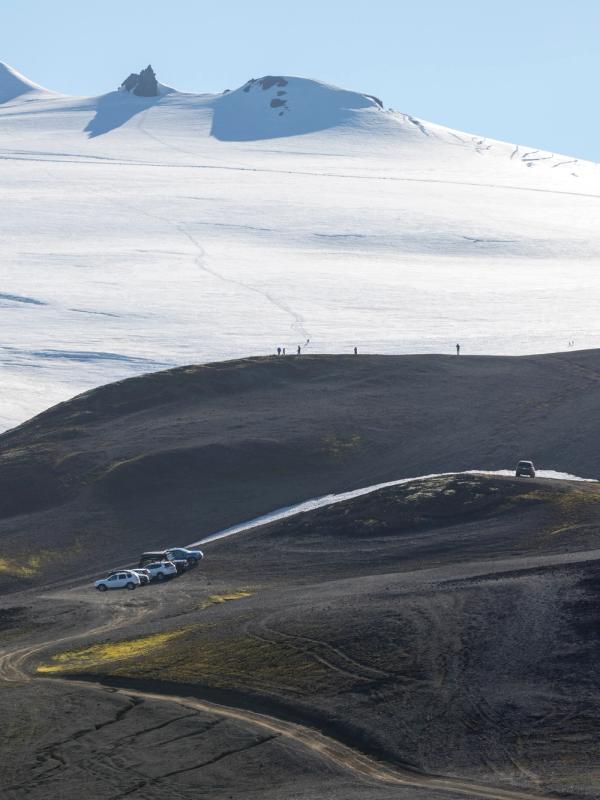 Glacier and dark volcanic hills with people and vehicles.