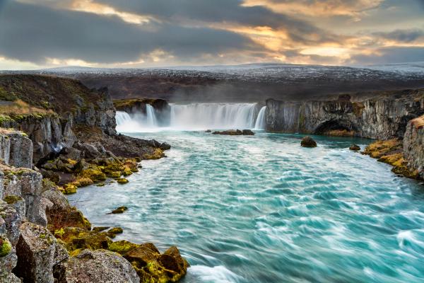 a waterfall in the middle of a river surrounded by rocks and mountains at Goðafoss in north Iceland.