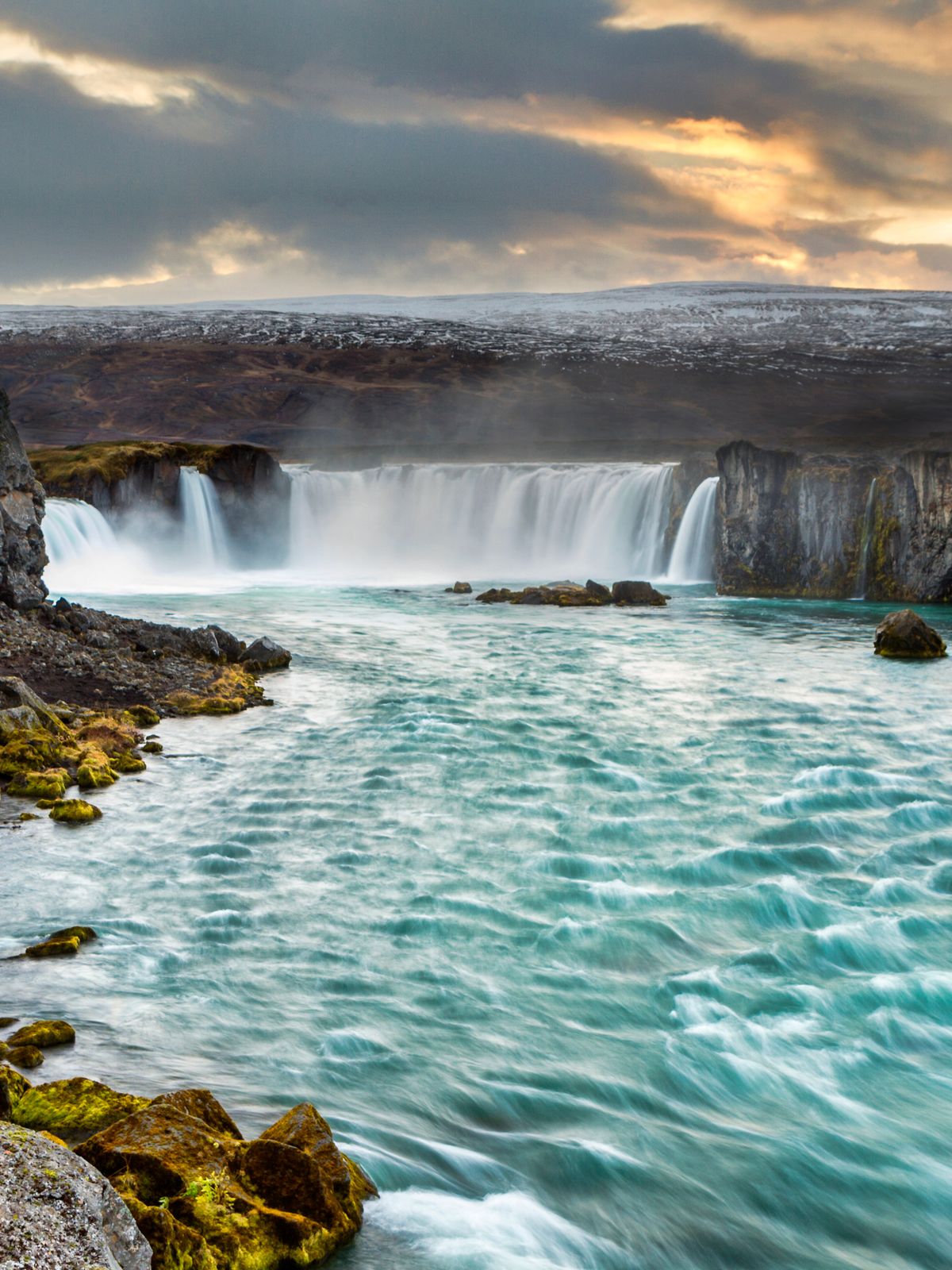 a waterfall in the middle of a river surrounded by rocks and mountains at Goðafoss in north Iceland.