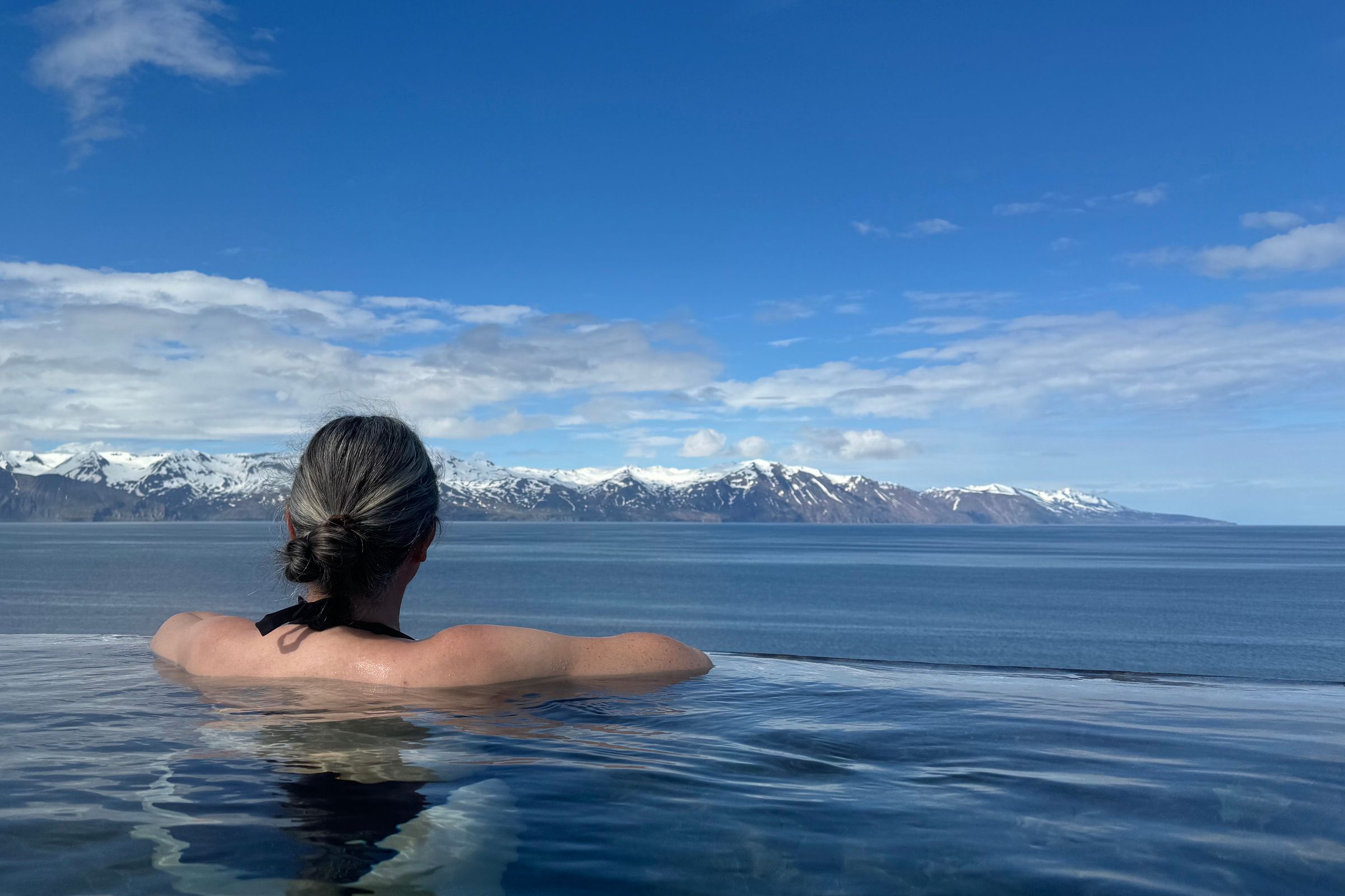 Woman in an infinity pool overlooking snow-capped mountains and the ocean.