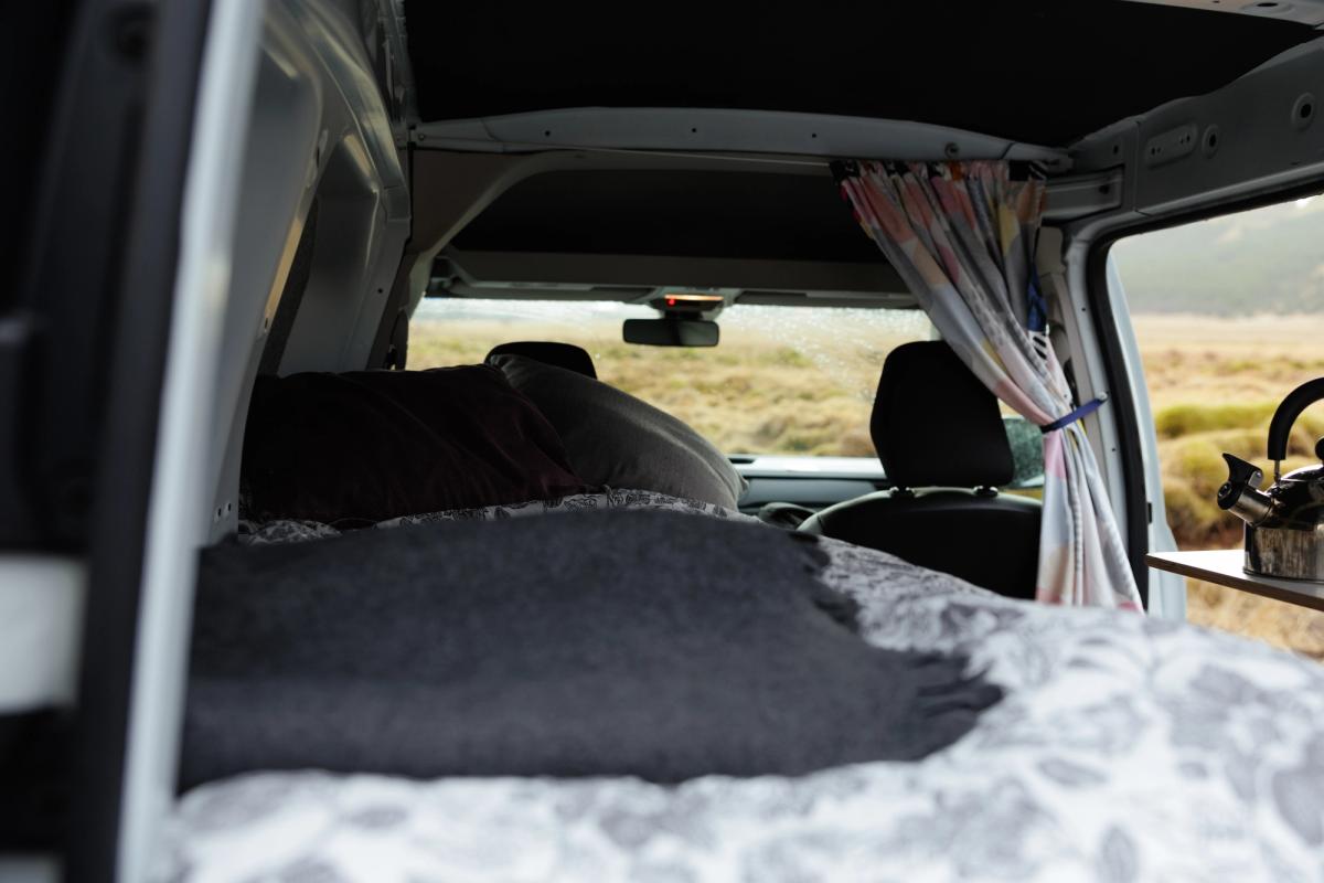 Bett mit einer dunklen Decke über der Bettdecke, mit Blick auf die Vordersitze und die Windschutzscheibe