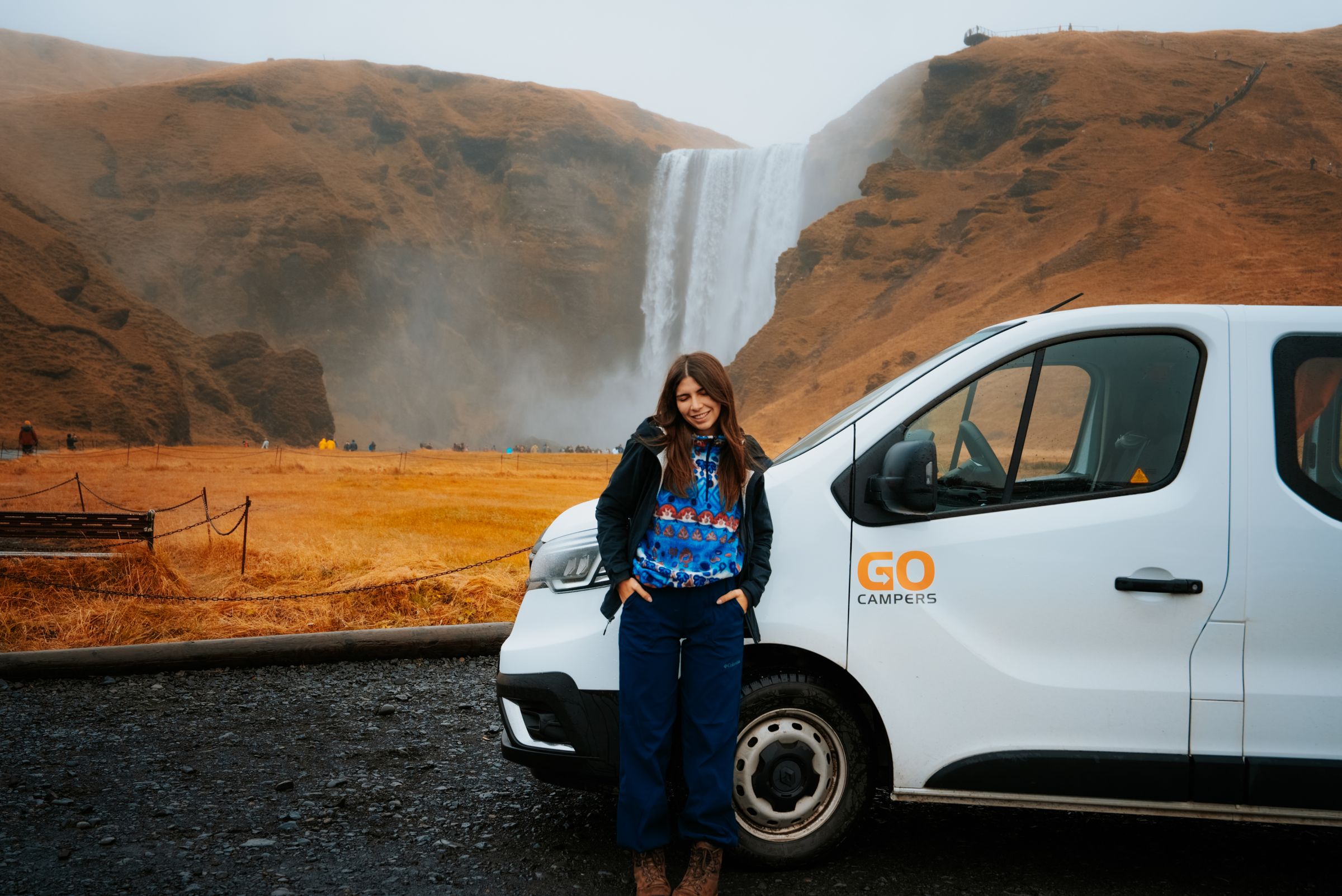 a woman is standing next to a white van in front of a waterfall .